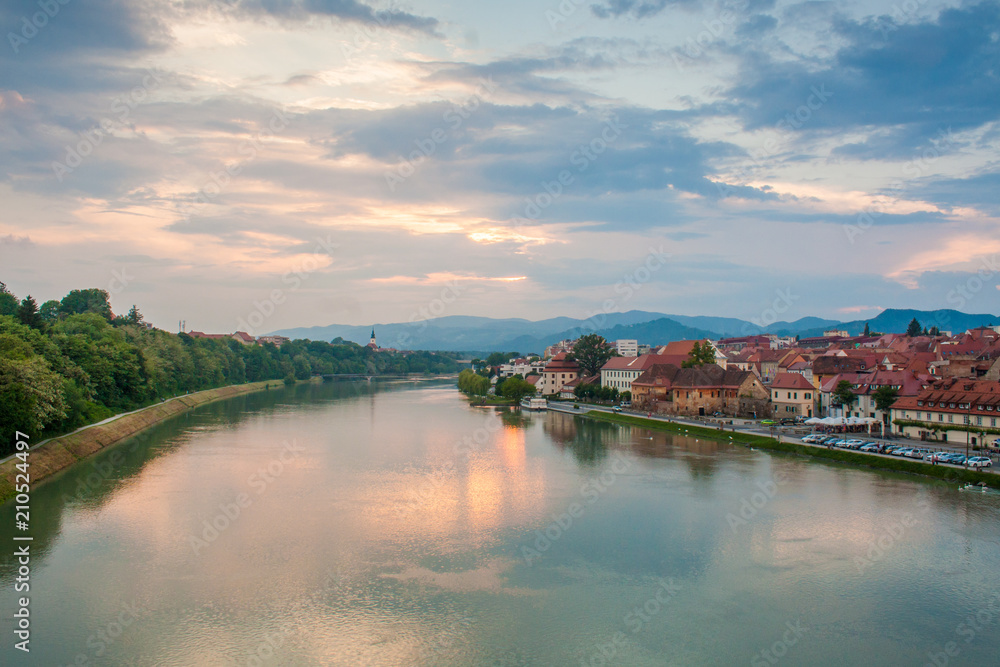 View of Maribor, Slovenia, Central Europe and the Lent area. Photo taken from Glavni most - bridge over the river Drava. Evening sky after sunset over colourful houses and a church in the distance.