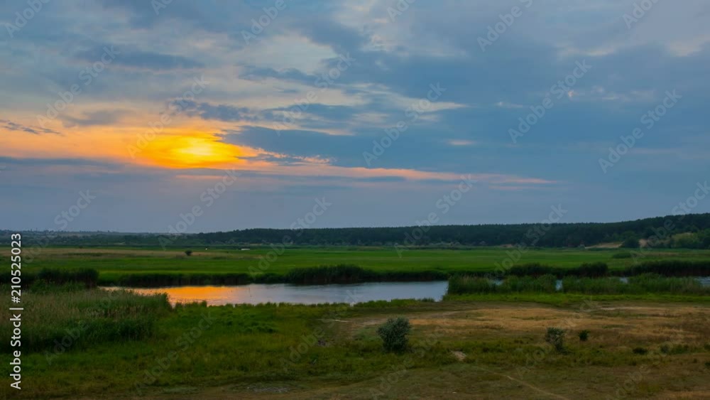 Timelapse sunset over river with reeds and forest under blue clouds Timelapse sunset over river with reeds and forest under blue clouds