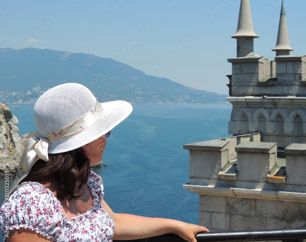 Woman in a hat looking at the castle swallow's nest and the sea in the Crimea    