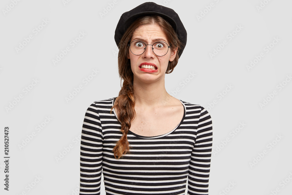 Nervous depressed young Parisian female in french clothing, looks with displeased expression, has discontent face, feels averse isolated over white studio wall. Negative human emotions concept. Nervous depressed young Parisian female in french clothing, looks with displeased expression, has discontent face, feels averse isolated over white studio wall. Negative human emotions concept.
