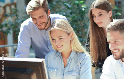 Group of young people in casual wear sitting at the office desk and discussing something while looking at PC together. photo