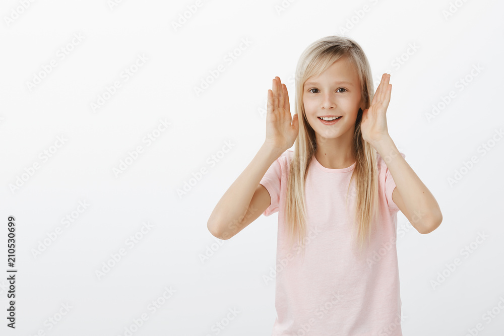 Adorable little girl showing dance moves she learnt. Portrait of active happy young european child with fair hair, holding hands near face and smiling broadly, making funny gestures, having fun Adorable little girl showing dance moves she learnt. Portrait of active happy young european child with fair hair, holding hands near face and smiling broadly, making funny gestures, having fun