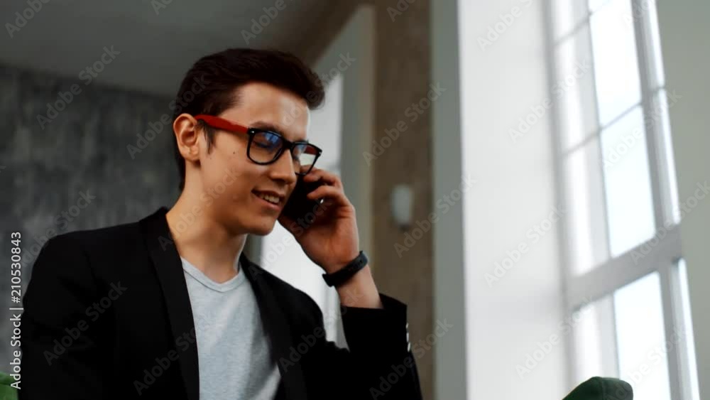 A young man with glasses answers the call, talking on the phone and smiling A young man with glasses answers the call, talking on the phone and smiling