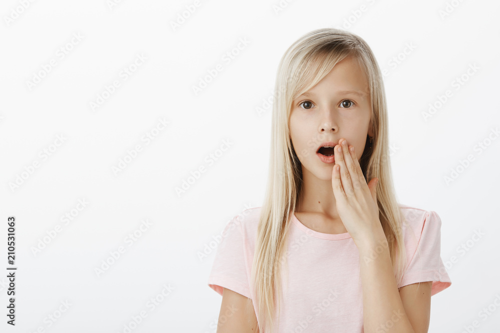 Shocked cute european girl with blond hair, spreading rumors or gossips in classroom, holding palm near mouth while whispering so nobody else will hear secret, standing serious over gray wall Shocked cute european girl with blond hair, spreading rumors or gossips in classroom, holding palm near mouth while whispering so nobody else will hear secret, standing serious over gray wall