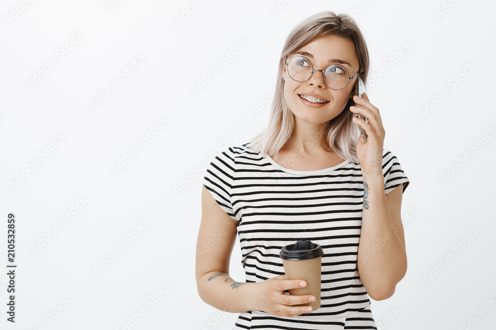 Come and pick me up in local cafe. Stylish relaxed good-looking woman with fair hair in glasses, holding cup of coffee, smiling and gazing aside while talking on smartphone, making plans for evening Come and pick me up in local cafe. Stylish relaxed good-looking woman with fair hair in glasses, holding cup of coffee, smiling and gazing aside while talking on smartphone, making plans for evening