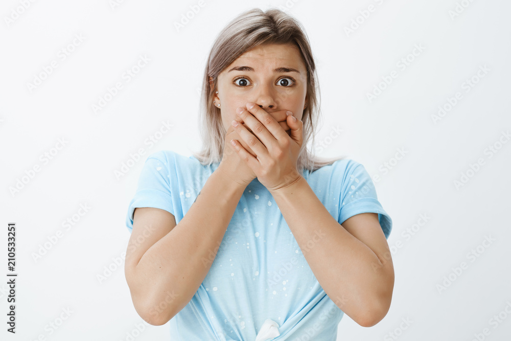 Gosh, it is terrible. Portrait of stunned and shocked charming teenage girl in light blue t-shirt, gasping, wanting so scream and covering mouth with palms, staring with worried look at camera Gosh, it is terrible. Portrait of stunned and shocked charming teenage girl in light blue t-shirt, gasping, wanting so scream and covering mouth with palms, staring with worried look at camera
