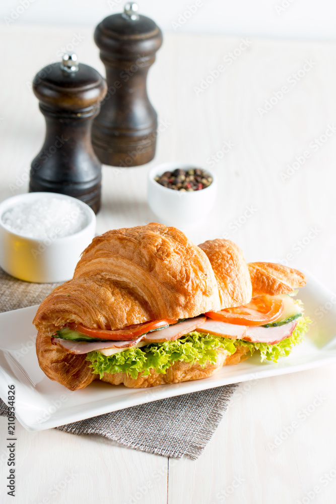Fresh croissant or sandwich with salad, ham, jamon, prosciutto, salami, cheese, chicken, tomatoes on wooden background. Morning breakfast concept. Healthy and fast food. Fresh croissant or sandwich with salad, ham, jamon, prosciutto, salami, cheese, chicken, tomatoes on wooden background. Morning breakfast concept. Healthy and fast food.