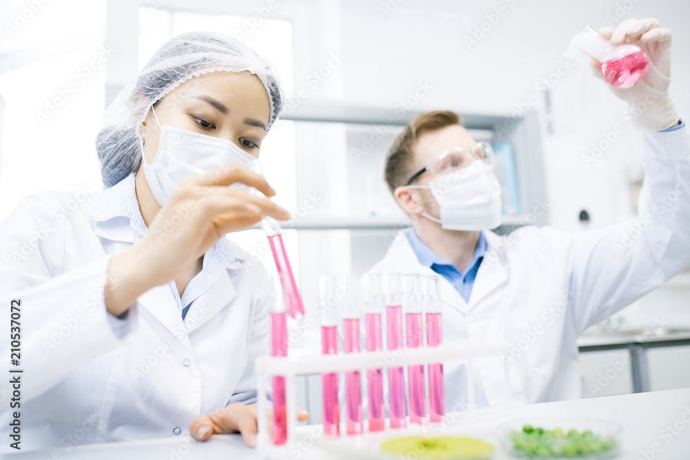Crop view of scientists sitting with test tubes and flask with pink liquid conducting laboratory experiments with meat Crop view of scientists sitting with test tubes and flask with pink liquid conducting laboratory experiments with meat