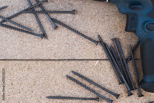 Top view of the elctric screwdriver with black metallic srews on the wooden table. Background with copy space on the hobby, DIY, hand tools, house repairing theme. photo