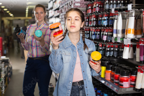 portrait of mother and daughter choosing paint color in jar in art shop