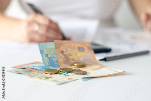Euro banknotes and golden coins on a desk in front of a working female secretary