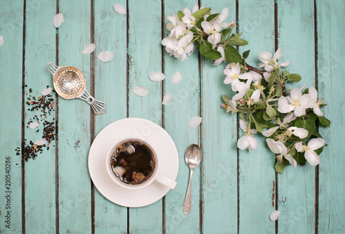 Apple tree blossom branch and a cup of tea with silver spoon and tea strainer on rustic wooden background, Valentines Day or Mothers day background, top view.