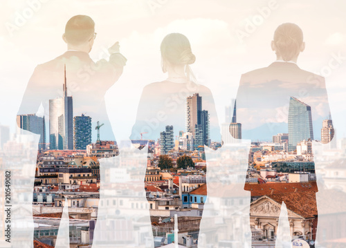 Silhouettes of business people standing back on the modern cityscape background with skyscrapers in Milan. Double exposure image technic