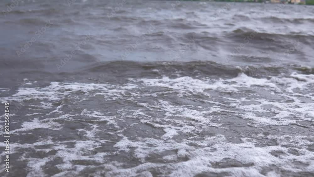 Dark turbid waves with white foam carry to the pebble shore a small debris after the storm. Dark turbid waves with white foam carry to the pebble shore a small debris after the storm.