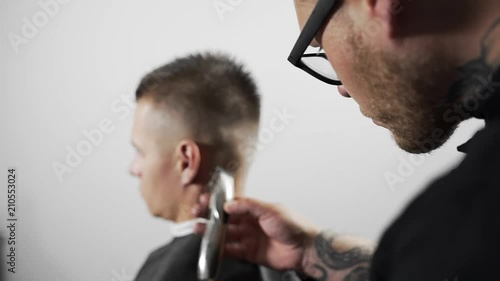 Tattoed barber makes haircut for customer at the barber shop by using hairclipper, man's haircut and shaving at the hairdresser, barber shop photo