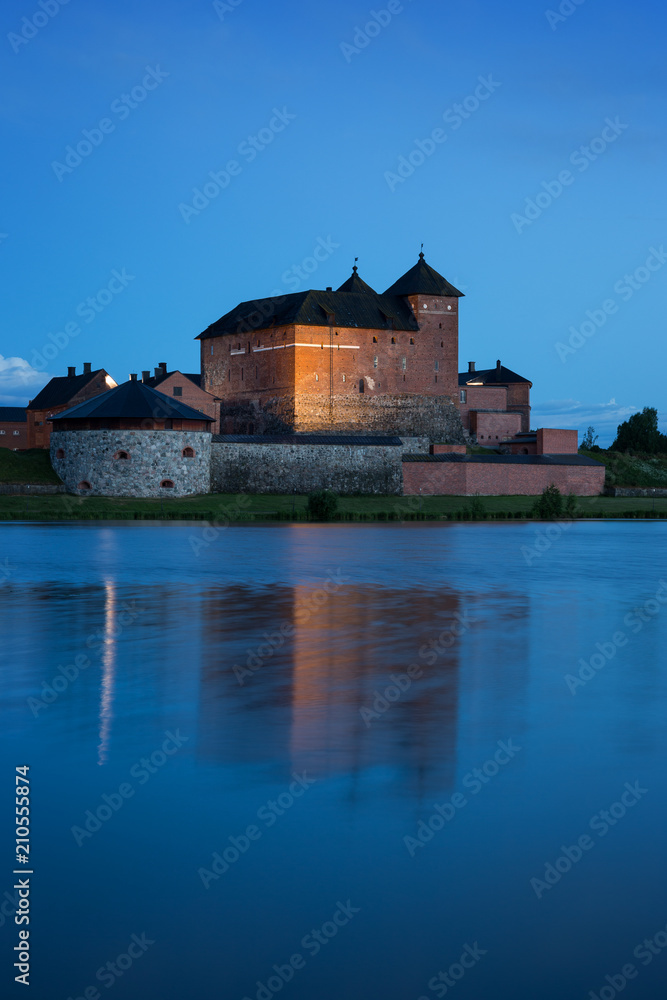 Beautiful view of lit 13th century Häme Castle and its reflections on lake Vanajavesi in Hämeenlinna, Finland, in the evening.
