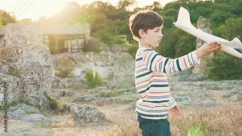 Slow motion а happy boy is playing with a toy airplane, standing on a beautiful landscape with large stones at sunset in the spring. Sun rays in green nature. Happy moments of life style