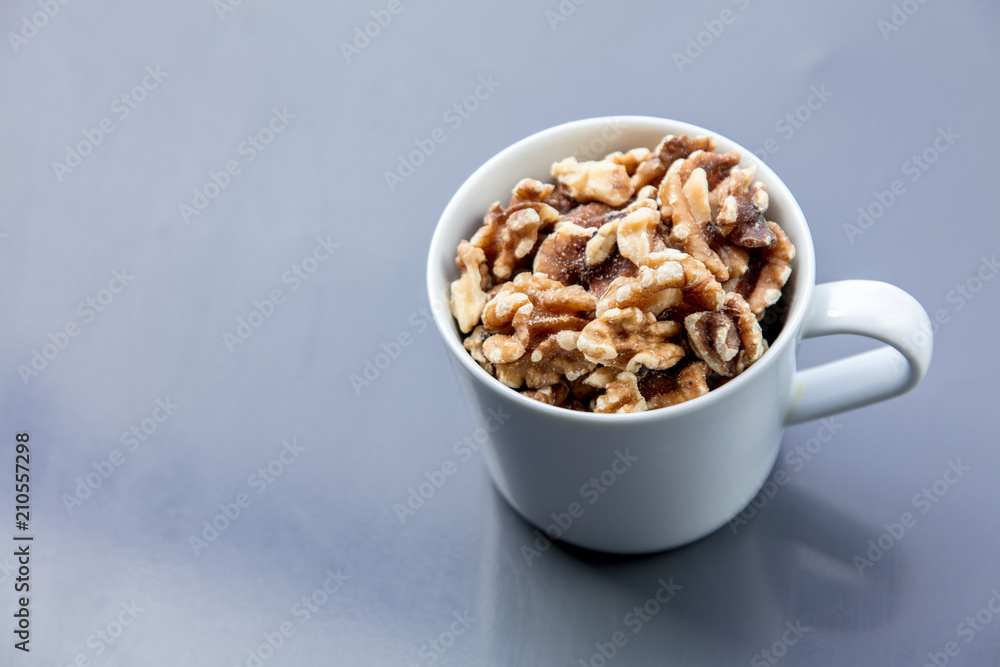 White cup full of walnuts on grey background. Above view White cup full of walnuts on grey background. Above view