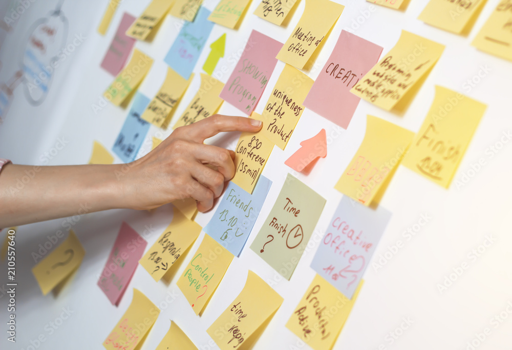 Business woman points a hand to a note on the wall, discussing the idea with co-workers. Business woman points a hand to a note on the wall, discussing the idea with co-workers.