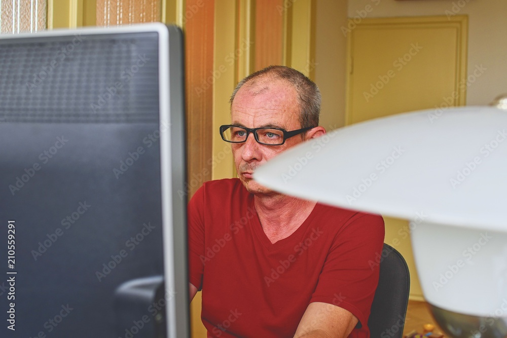 Fototapeta premium Middle aged man with glasses sitting at desk. Mature man using personal computer. Senior concept