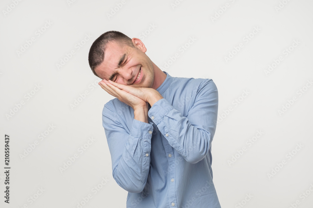 Young man wearing a blue outfit putting his palms like a pillow. Looking sleepy and tired. Young man wearing a blue outfit putting his palms like a pillow. Looking sleepy and tired.