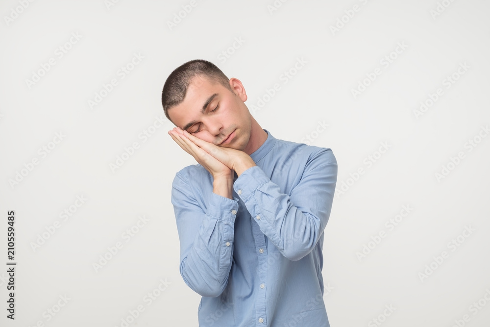 Young man wearing a blue outfit putting his palms like a pillow. Looking sleepy and tired. Young man wearing a blue outfit putting his palms like a pillow. Looking sleepy and tired.