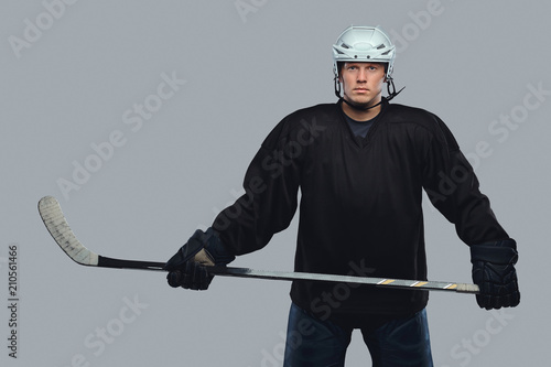 Canvas Print Hockey player wearing black protective gear and white helmet holds a hockey stick on a gray background