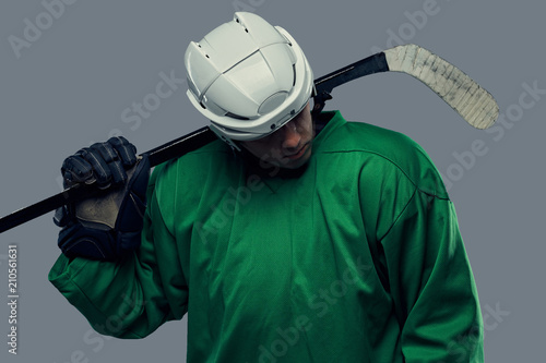 Canvas Print Hockey player wearing green protective gear and white helmet standing with the hockey stick
