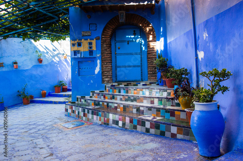 Blue walls of Chefchaouen city medina in Morocco with bright doors and colorful flower pots on the walls with sun light © siv2203