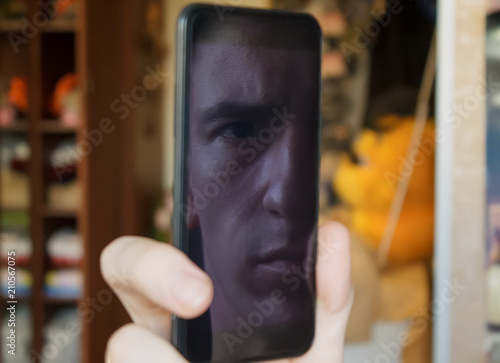 guy looks at the screen of a black smartphone, through the reflection of the screen looks one eye into the camera