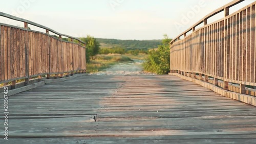 Slow motion wiring an ancient wooden bridge across a deep gorge in the background of a beautiful sunset. The bridge is made of hard wooden boards. Beautiful warm rays of the sun. Hilly landscape