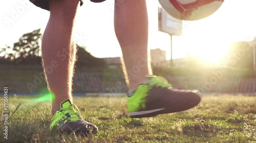 Slow motion football stunts. The football player throws the ball alternately with his feet. A teenager is playing on an abandoned football field at sunset on a sunny day in the summer. Football field