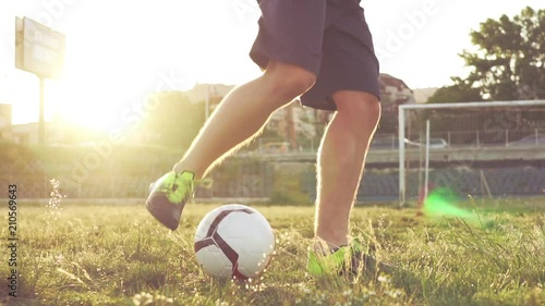 Slow motion football stunts. The football player throws the ball alternately with his feet. A teenager is playing on an abandoned football field at sunset on a sunny day in the summer. Football field
