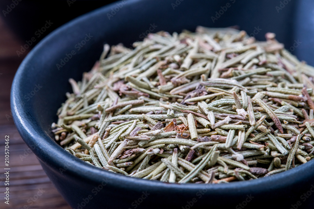 Dried Rosemary herb in black bowl close up