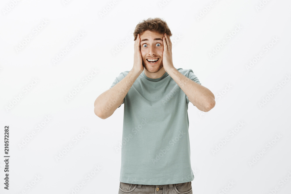 Portrait of excited crazy european guy in t-shirt, holding hands on face and smiling with weird funny expression, being happy and overwhelmed with positive emotions hearing great news Portrait of excited crazy european guy in t-shirt, holding hands on face and smiling with weird funny expression, being happy and overwhelmed with positive emotions hearing great news