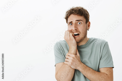 Фотография Studio shot of intense afraid handsome male feeling scared and shocked, biting f