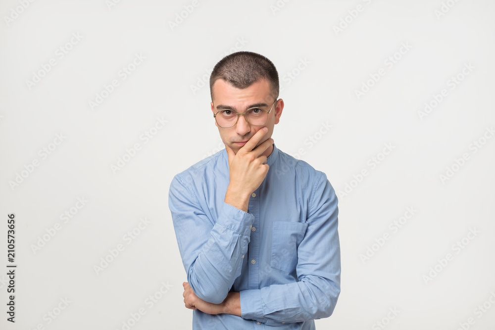 Young man in blue shirt standing disorientated bewildered isolated on gray wall background. Decision making concept. Young man in blue shirt standing disorientated bewildered isolated on gray wall background. Decision making concept.