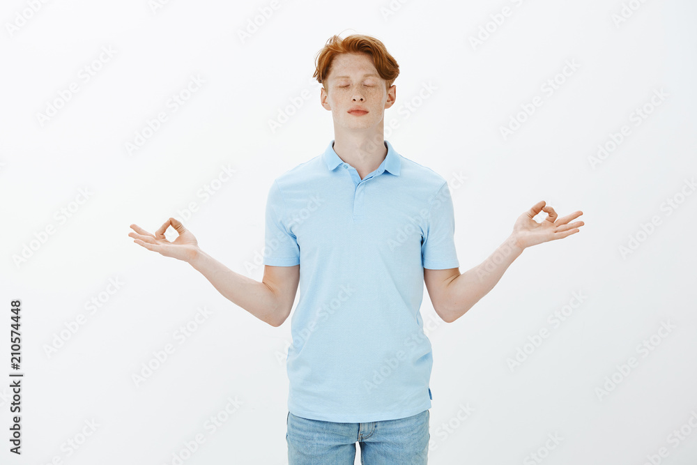 Calm down, need some relaxation. Studio shot of handsome redhead male student with freckles and tattos, standing with closed eyes and spread hands in zen gesture, meditating or practicing yoga Calm down, need some relaxation. Studio shot of handsome redhead male student with freckles and tattos, standing with closed eyes and spread hands in zen gesture, meditating or practicing yoga