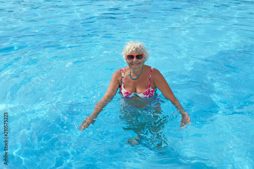 Aged woman is doing spa exercises in bright blue water of pool. © vaz1