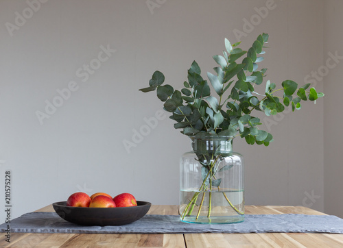 Fototapeta Naklejka Na Ścianę i Meble -  A bunch of twigs of eucalyptus and a plate of apples on a wooden table.