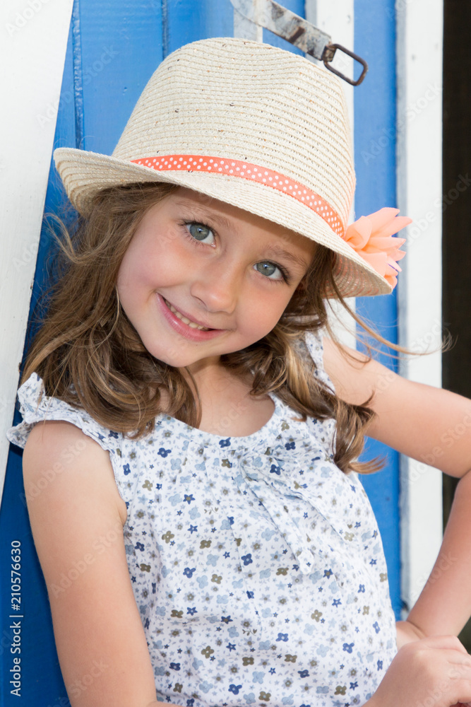 Smiling cute child girl 4-5 year old wearing flowers dress clothes posing in garden outdoors with straw hat
