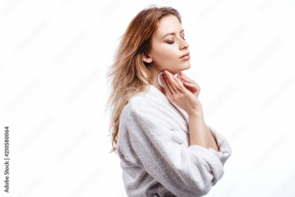 Young woman in a bathrobe cleans the face with cotton pads, spa and care portrait, clean natural face, portrait on a white background isolated