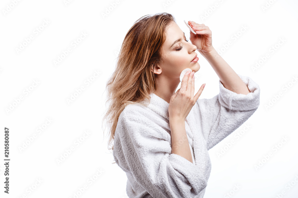 Young woman in a bathrobe cleans the face with cotton pads, spa and care portrait, clean natural face, portrait on a white background isolated Young woman in a bathrobe cleans the face with cotton pads, spa and care portrait, clean natural face, portrait on a white background isolated
