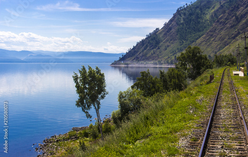 Bright summer landscape with Circum-Baikal railway on shore lake Baikal. Blurred foreground from train movement