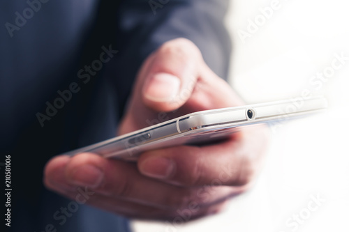 Close Up Of A Businessman Touching A Mobile Phone In Front Of A Bright Background