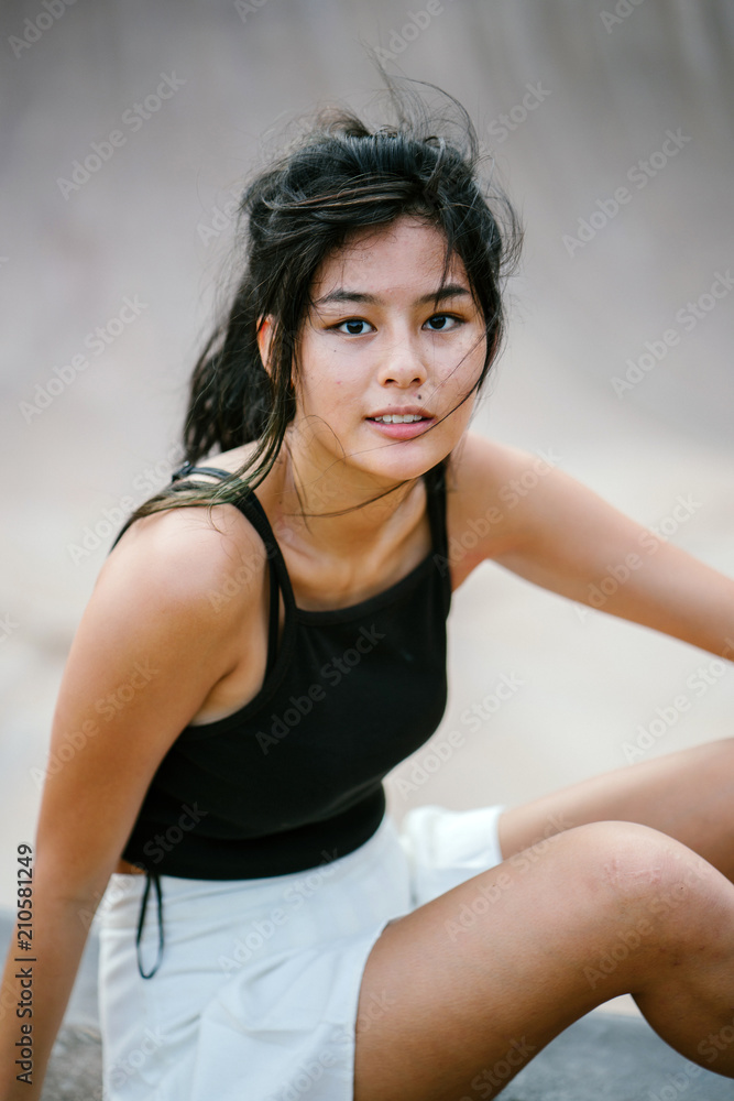 A headshot of a pretty and young Chinese Asian skater girl smiling glamorously in front of the camera. She is sitting on the ground at a skate park. A headshot of a pretty and young Chinese Asian skater girl smiling glamorously in front of the camera. She is sitting on the ground at a skate park.