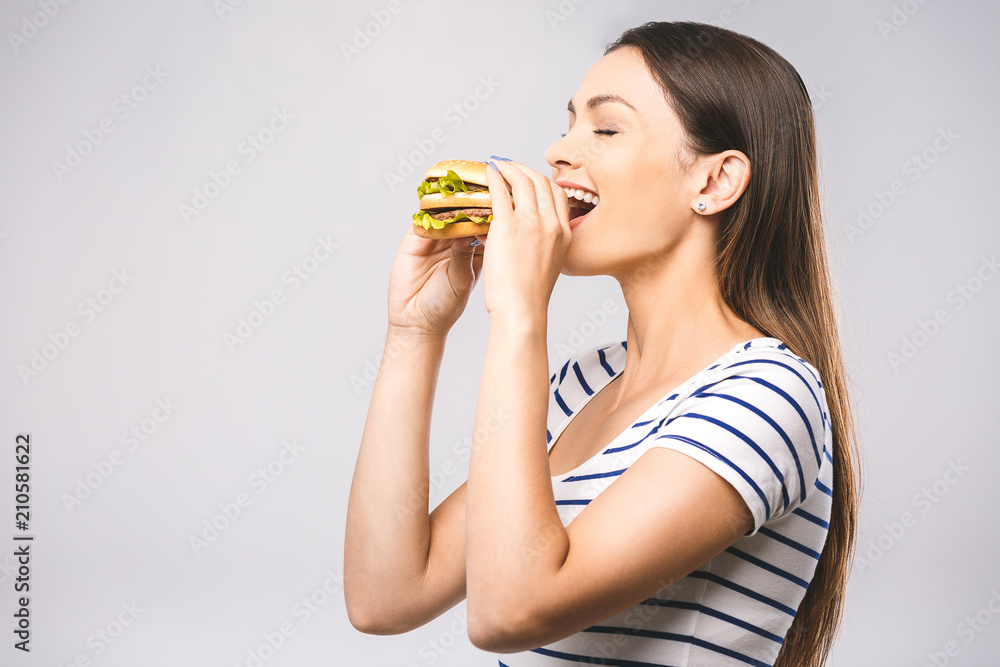 Young happy beautiful woman eating hamburger woman eating junk food, fatty food hamburger. White background, close-up, isolated. Diet concept. Young happy beautiful woman eating hamburger woman eating junk food, fatty food hamburger. White background, close-up, isolated. Diet concept.