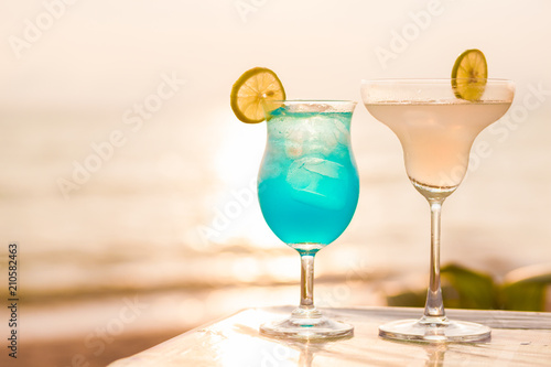 two perfect cocktails Blue Hawaii and Margarita over sunset beach background