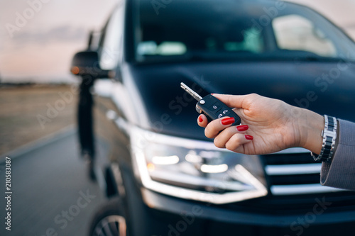 Woman is holding car keys in front of minivan
