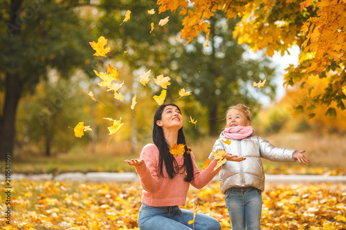 Cheerful girls playing with yellow leaves. Happy mother and little child in the fall time having fun